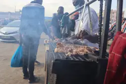 Man Standing Next To A Grill With A Bunch Of Food