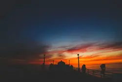 Sunset With A Lighthouse And A Person Standing On A Bench