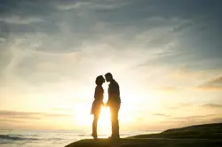 Two People Standing On A Beach With A Sun Set