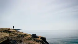 Person Sitting On A Rock Near A Body Of Water
