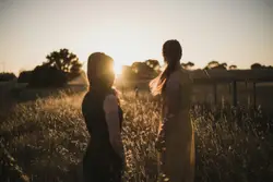 Two People Standing In A Field With A Sun Set
