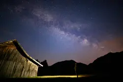 Person standing near barn under starry night
