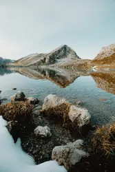 Brown rocky mountain beside lake under blue sky during 