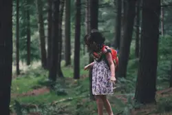 Girl walking in field surrounded with tall and green tr