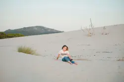 Girl in white shirt sitting on white sand during daytim