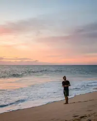 Woman in black dress standing on beach during sunset