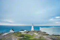 Lighthouse on cliff near fence and house