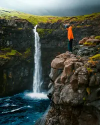 Person standing on rock formation watching waterfall du